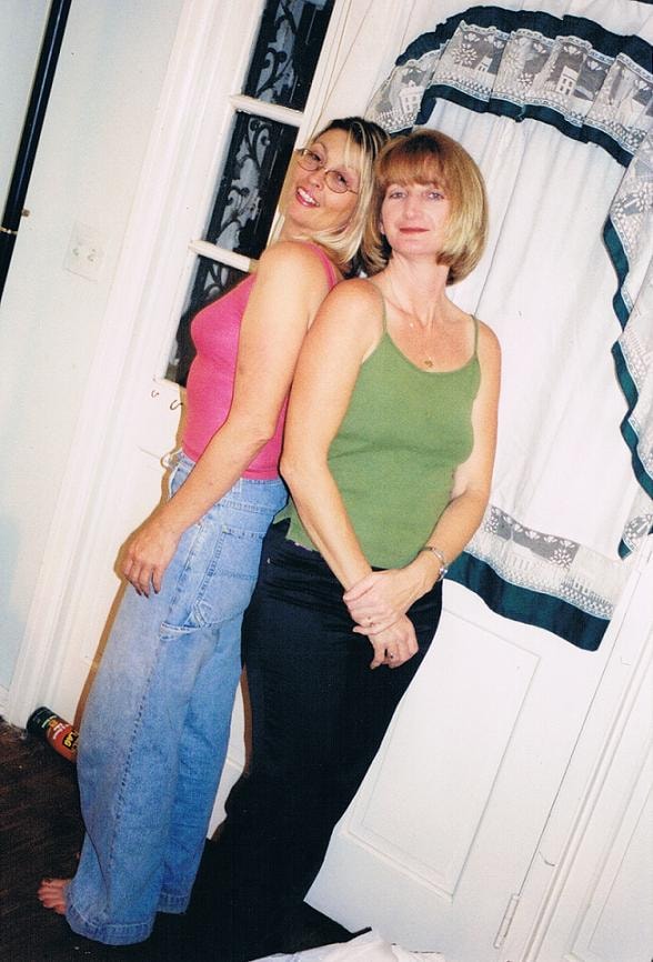 Two women posing back to back indoors