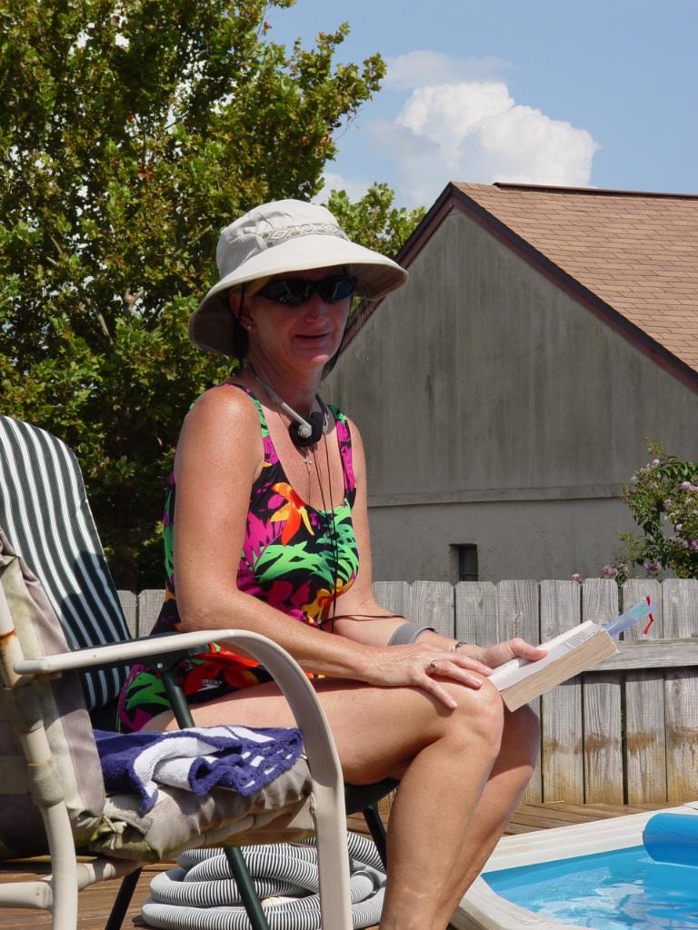 Woman reading book by pool in sun hat