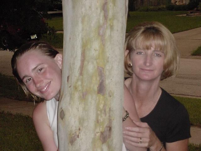 Two women peeking around tree trunk at night