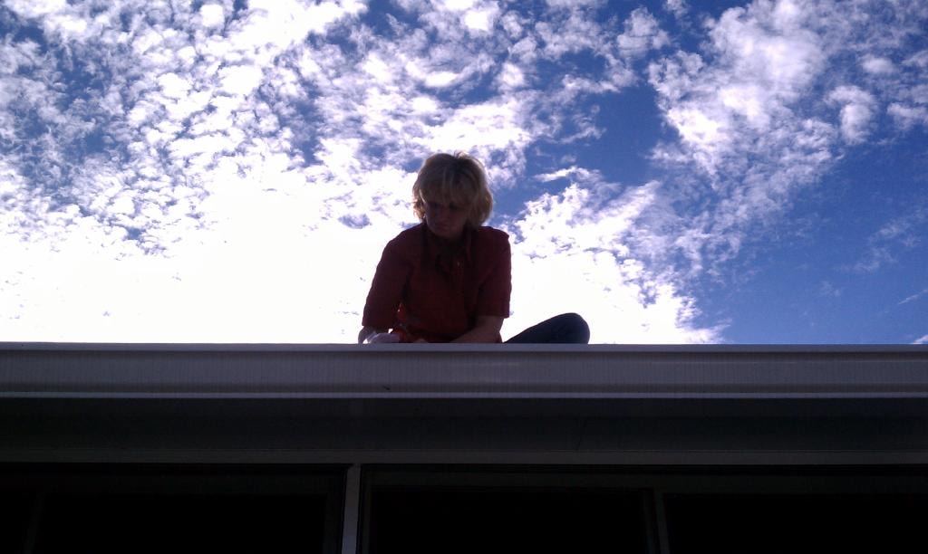 Woman sitting on rooftop against blue cloudy sky