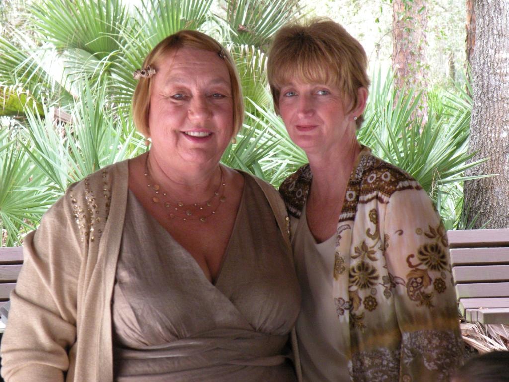 Two women sitting together outdoors tropical palms