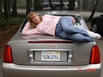 Woman lying on hood of Cadillac in forest