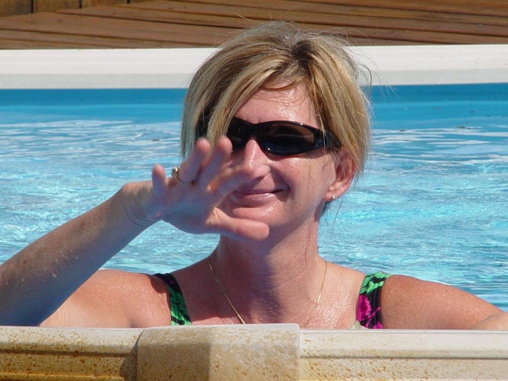 Woman waving from pool wearing sunglasses