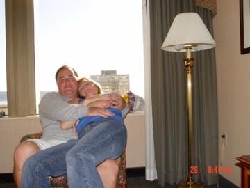 Couple cuddling in hotel room chair by window city view