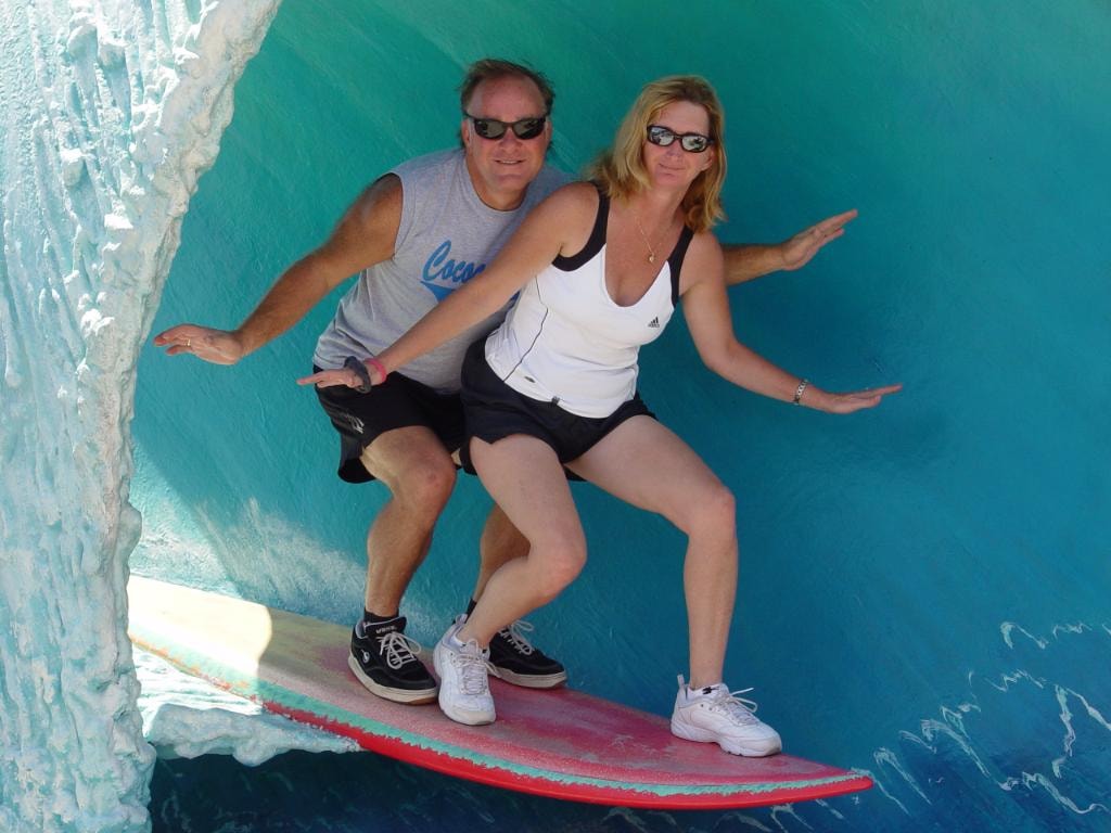 Couple posing on surfboard display turquoise wave backdrop